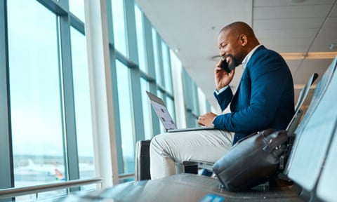 An African businessman having a mobile phone conversation in the airport, waiting to board his flight. He has a laptop in front of him, working.