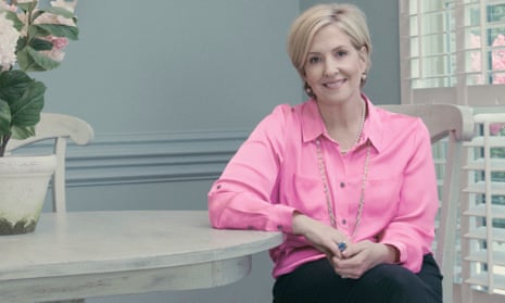 Brené Brown, smartly dressed and sitting sideways at a table, smiling at the camera