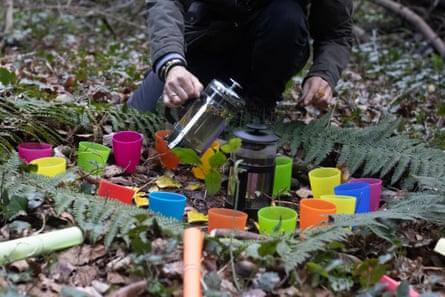 A personification pours beverage from a gallic property into a bunch of colorful cups successful nan forest