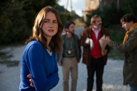 A girl wearing a sky-blue sweater over a light-blue T-Shirt, and three men in the background