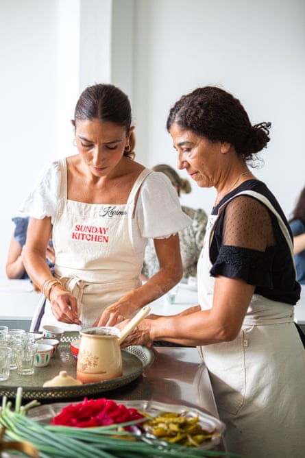 A mother and daughter in white aprons, preparing a pot of Lebanese coffee.