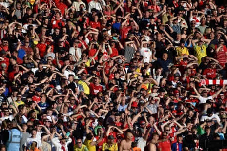 Fans shield their eyes from the sun as they watch the English Premier League soccer match between Nottingham Forest and Arsenal at City Ground .