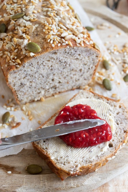A loaf of seeded bread with a slice cut, and spread with butter and jam