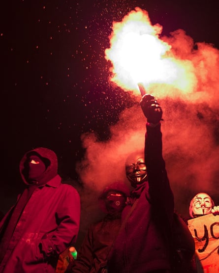 Masked protesters hold a flare as they stand on Nelson’s Column