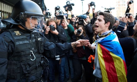 A man wrapped in the Catalan flag faces a riot police officer during a protest in Barcelona over the arrest of Carles Puigdemont.
