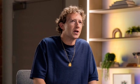 a man wearing a blue T-shirt speaks as he sits on a chair
