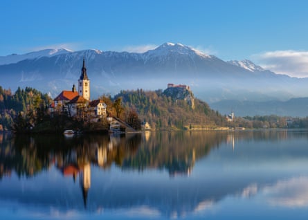 Sunny day view across Lake Bled in north-western Slovenia, with the Pilgramage Church of the Assumption of Maria on the lake shores, and mountains in the background, all reflected in the water