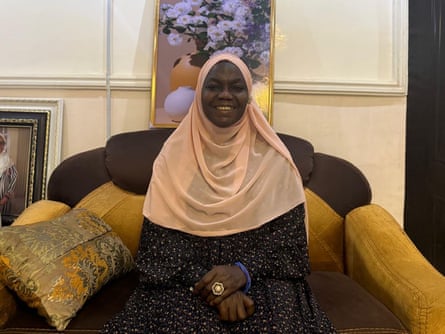 A Nigerian woman smiling in an armchair wearing traditional head covering