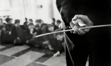 Teacher wielding cane behind his back in 1960s school