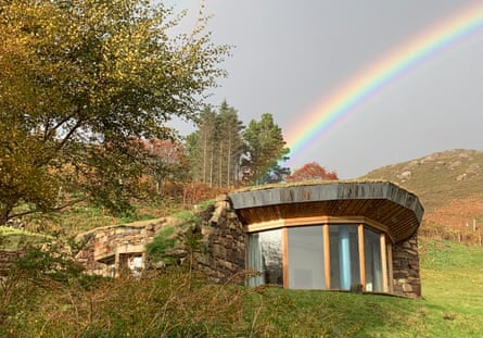 Stone building with large windows pictured against mountains and a rainbow.