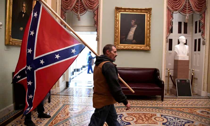 Un hombre lleva una bandera de batalla confederada en el segundo piso del Capitolio de los Estados Unidos.