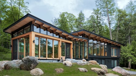 Modern flat-roofed glass building in forest setting with boulders in foreground