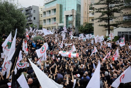 A large crowd of people carrying white Lebanese Forces flags in the streets of Byblos.