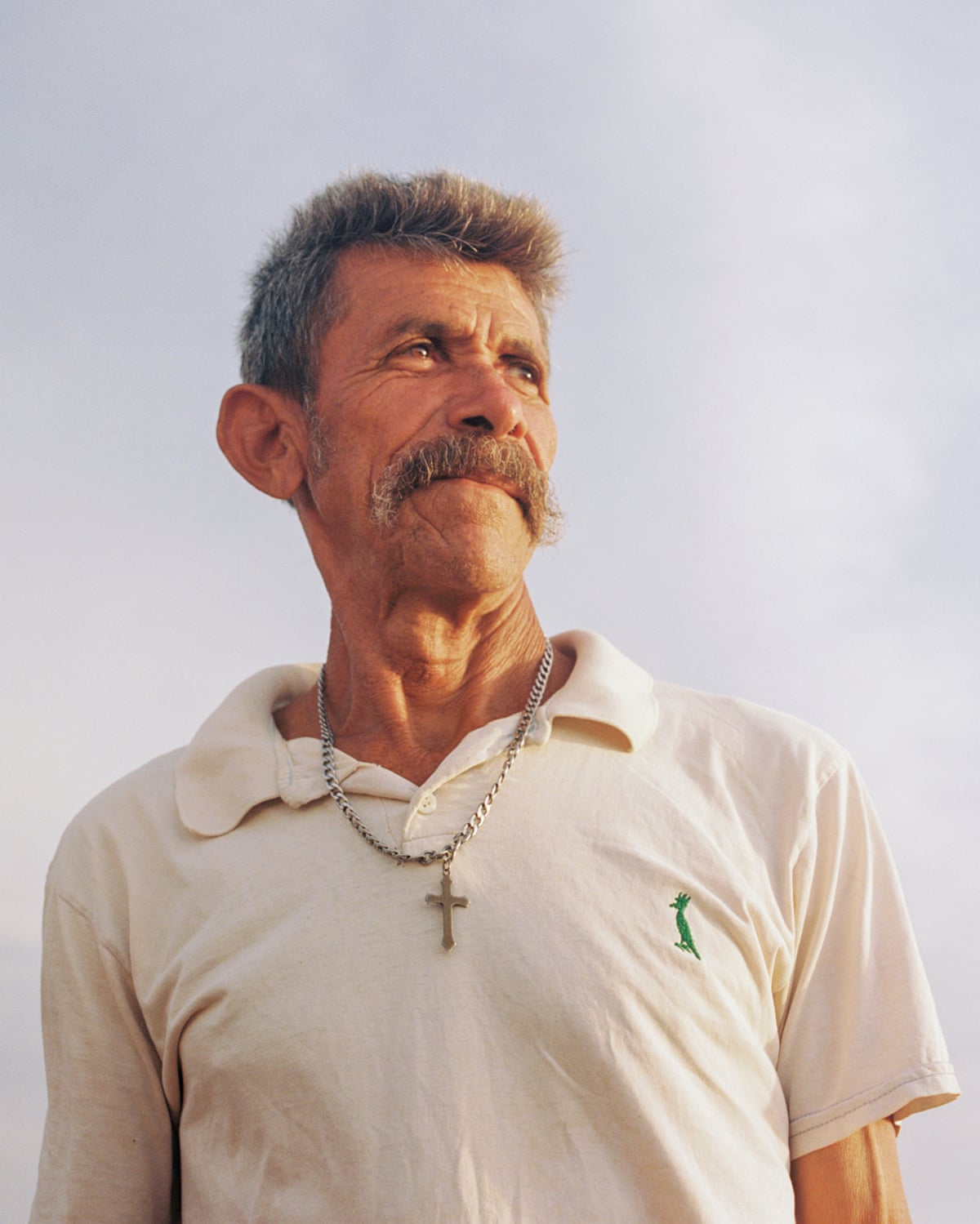 An older Hispanic man with a big moustache and a crucifix pendant looks away into the distance