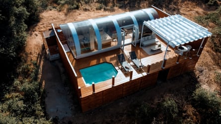 An overhead shot of a wooden platform with outdoor pool and seating area, and a transparent curved tube over the bedroom and bathroom areas