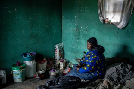 African woman looking downcast while sitting on a low bed in a poorly furnished room.