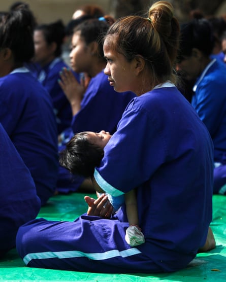 A woman in a blue uniform surrounded by other people in the same uniform. She is sitting on the ground holding a small child