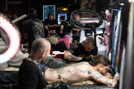 Tattooed man lies face down while tattooists work in the background