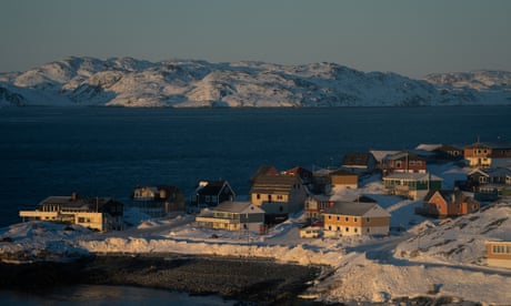 Quelques maisons sur un sol enneigé avec la mer et les collines enneigées derrière