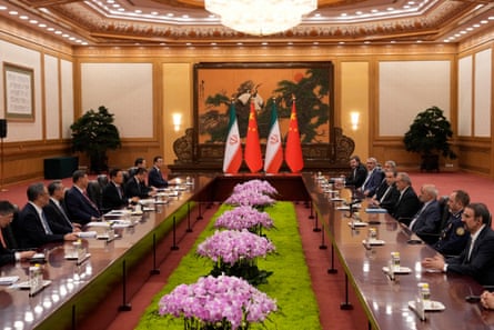 Xi Jinping and Masoud Pezeshkian sit flanked by officials in a large room with displays of flowers and the Chinese and Iranian flags