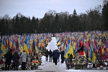 People visit a cemetery filled with flags and tributes around graves