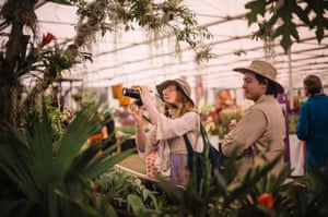 A woman takes a photo of a tropical plant with a large camera as a person beside her looks at the plant.