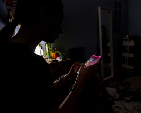 silhouette of a teenage girl sitting inside room on cellphone