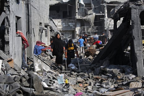 Palestinians walk through the rubble of a destroyed building.