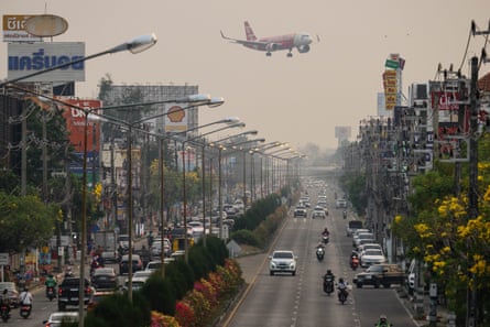 A passenger plane flies over a busy city street and prepares to land at the airport in Chiang Mai amid heavy pollution