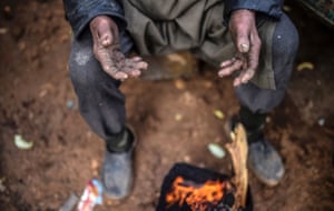 A man warms himself by a bonfire at a Turkish border crossing gate.