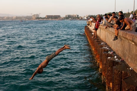 A young boy dives off a quay as men and other boys look on