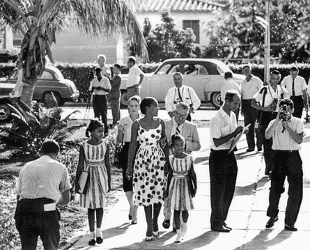 A Black woman walks with her two young childen through a throng of white people.