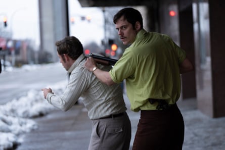 A man holds another man at gunpoint on a snowy US city street.