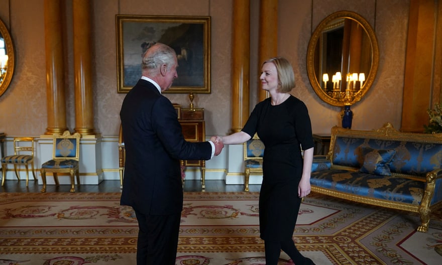 Charles and Truss, both wearing black, shaking hands in a large grand room