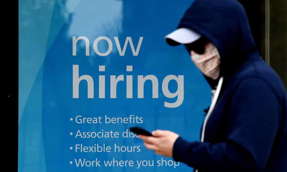 A sign outside a store in Arlington, Virginia announcing that jobs are available as a man in a face mask walks by
