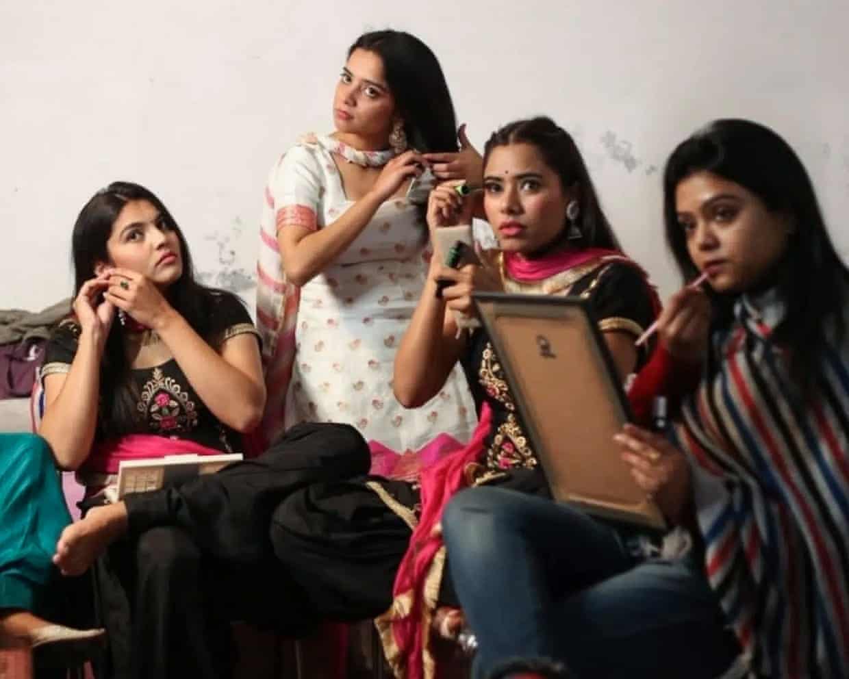 Four young women sitting side by side, applying makeup and doing their hair.