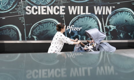 A woman pushes a baby in a pram past a sign outside Pfizer’s headquarters in New York