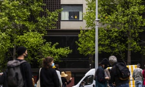 A person (top) looks out a window of the Park Hotel in Carlton as refugee advocates participate in a rally across the road