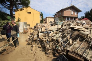 Volunteers clear mud as household goods are piled on the side of a street in Faenza