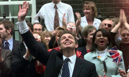 Tony Blair waves to well-wishers in Downing Street on 2 May 1997 as he became the new prime minister: he is seen in front of people who are waving and cheering; several are holding union jack flags, and he has one arm raised high; he is looking upward