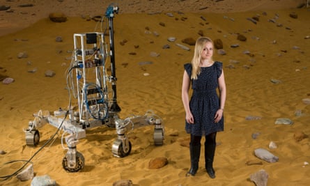 female engineer Abbie Hutty poses with metal Mars rover prototype on reddish sand