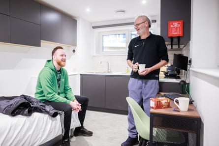 Two men in a newbuild flat, one sitting on the bed