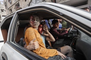A Palestinian girl whose face appears to be stained with blood or mud sits on the lap of a similarly stained man in a car