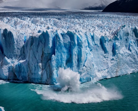water splashes from the green-blue lake as a large chunk of ice falls into it from the glacier