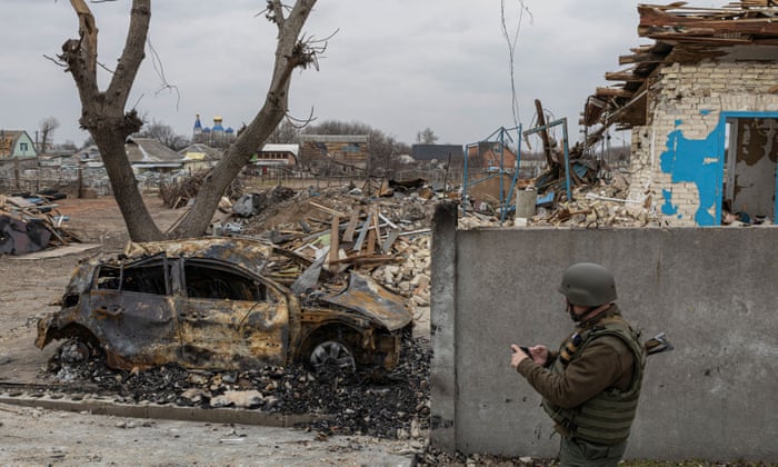 A Ukrainian serviceman walks past a burnt-out car in the village of Krasylivka outside Kyiv.
