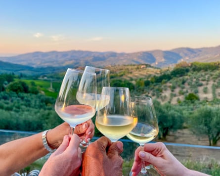 Group of people making a celebratory toast with Tuscany hills and vineyards in the background. White wine in the glasses at sunset. Multi ethnic group.