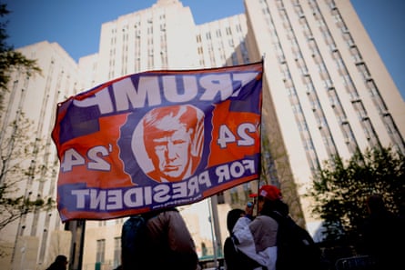 With a high-rise building in the background on a sunny day, a woman in a red baseball hat waves a red, white and blue flag with Trump's image on it, which says Trump '24 for President.