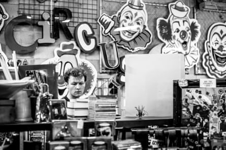 A black-and-white image of a man looking at items on shelves, with decals of circus clowns hanging on the wall behind him.