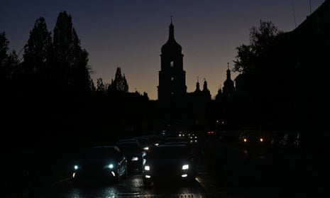 Vehicles drive along a street in Kyiv= on 31 October with the St Sophia Cathedral silhouetted in the background, as the city is plunged into near darkness following a military strike that partially brought down the power infrastructure.