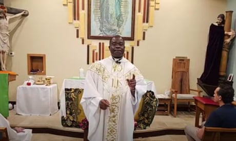 A priest wearing a white robe speaks in the front of a church
